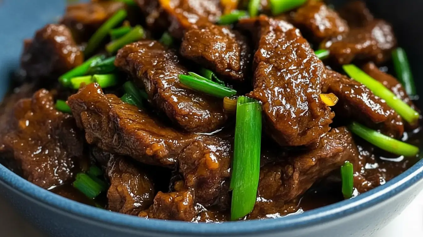 Slow cooker Mongolian beef served in a blue bowl, featuring tender beef strips coated in a glossy dark sauce, garnished with fresh green onions.