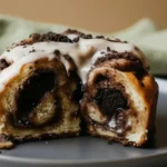 Cinnamon rolls with Oreo filling served on a plate, featuring soft swirled dough layered with crushed Oreo cookies, topped with a creamy vanilla glaze and cookie crumbs.