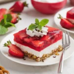 A slice of strawberry pretzel salad with a pretzel crust, creamy white filling, and strawberry gelatin topping, garnished with whipped cream and fresh strawberries