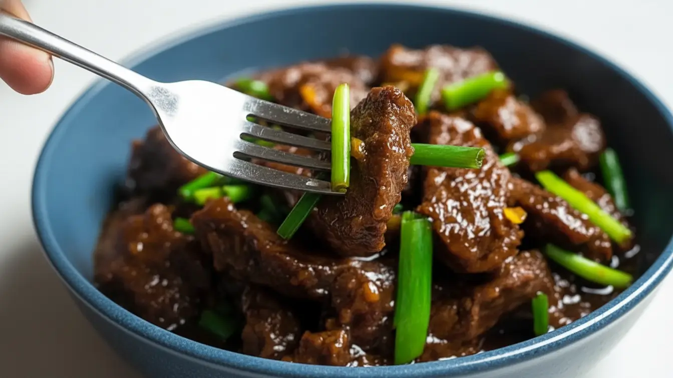 Whisk_cb7a031df36849181b44738db0a10d09eg Slow cooker Mongolian beef served in a blue bowl, featuring tender beef strips coated in a glossy dark sauce, garnished with fresh green onions.